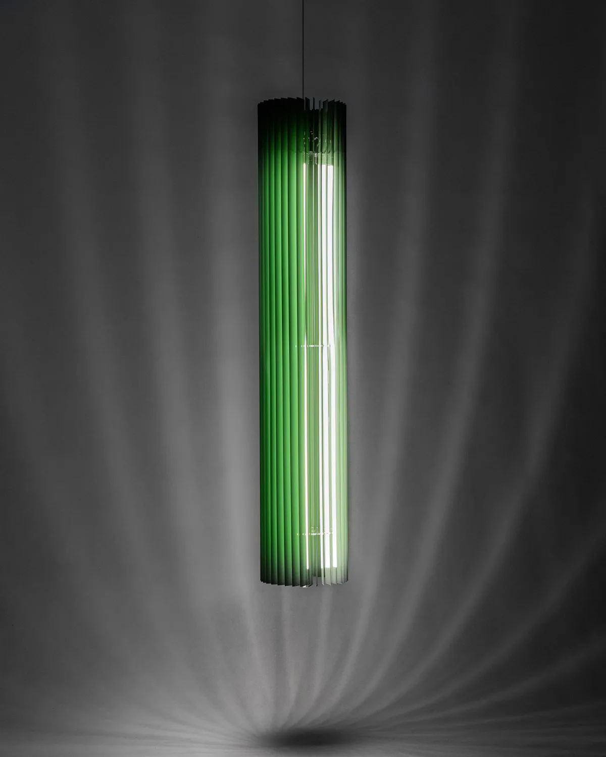 Keker pendant glowing green against grey, its pleats casting radial shadows
