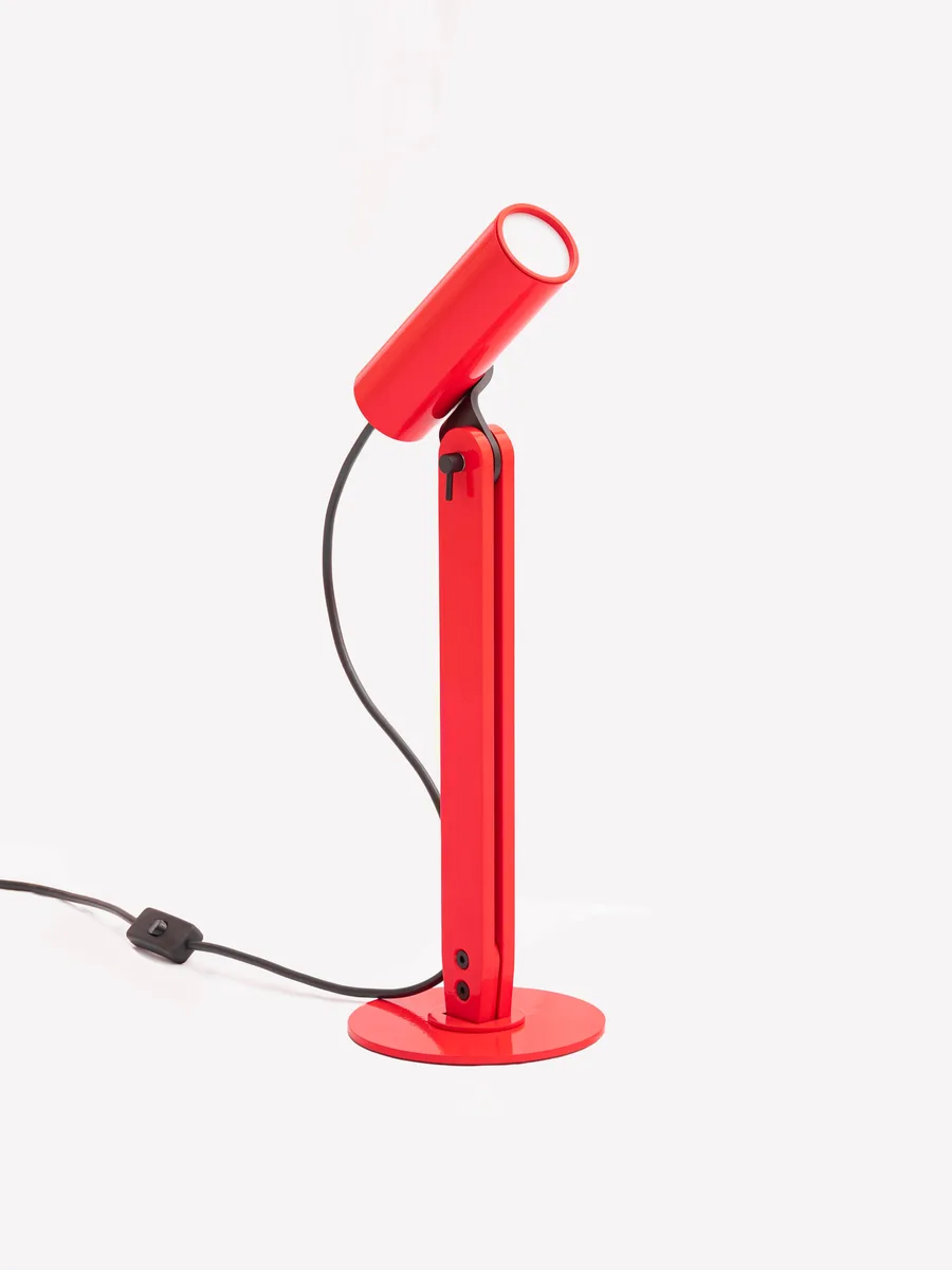 The Arte table lamp in red, its cylindrical head tilted skyward