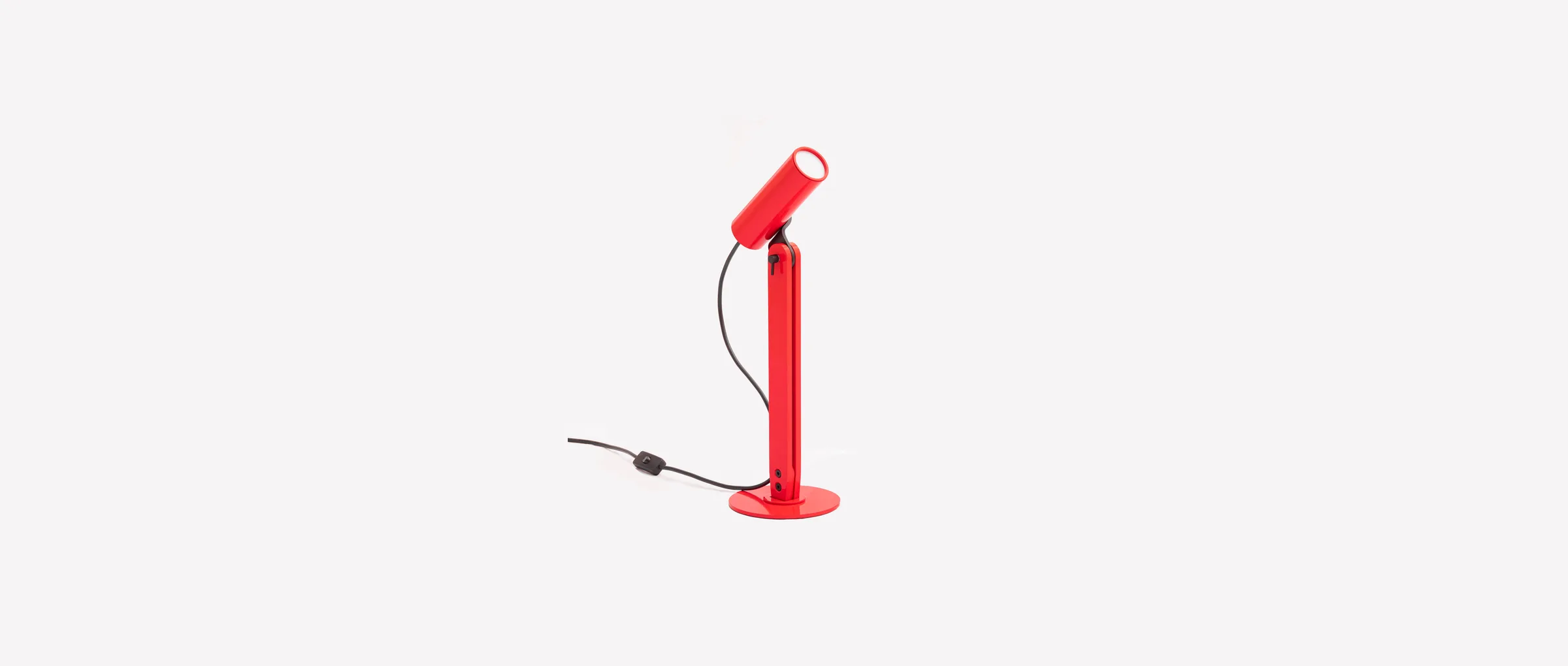 The Arte table lamp in red, its cylindrical head tilted on the flat stem
