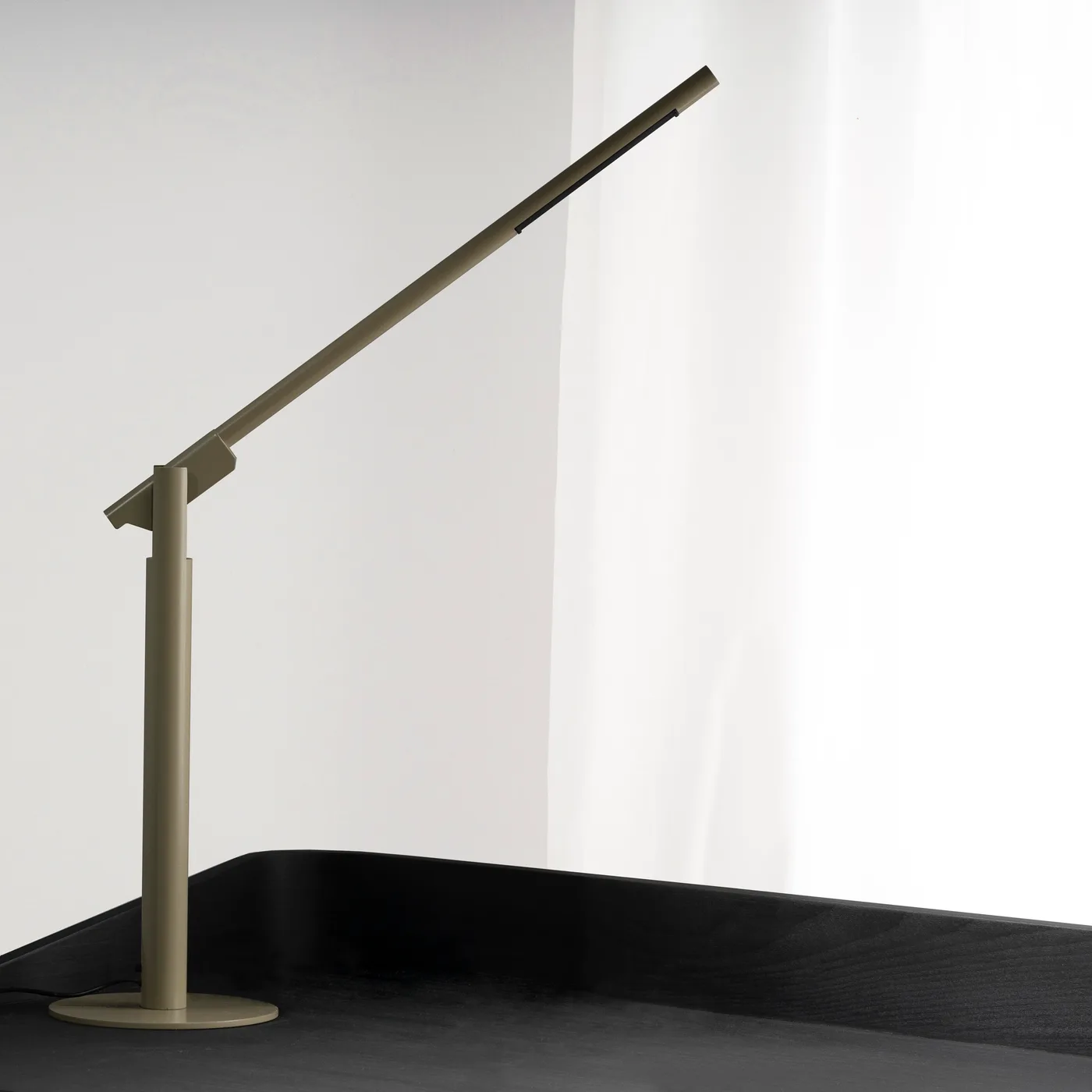 A khaki Calibre on a black desk, arm angled toward the window light