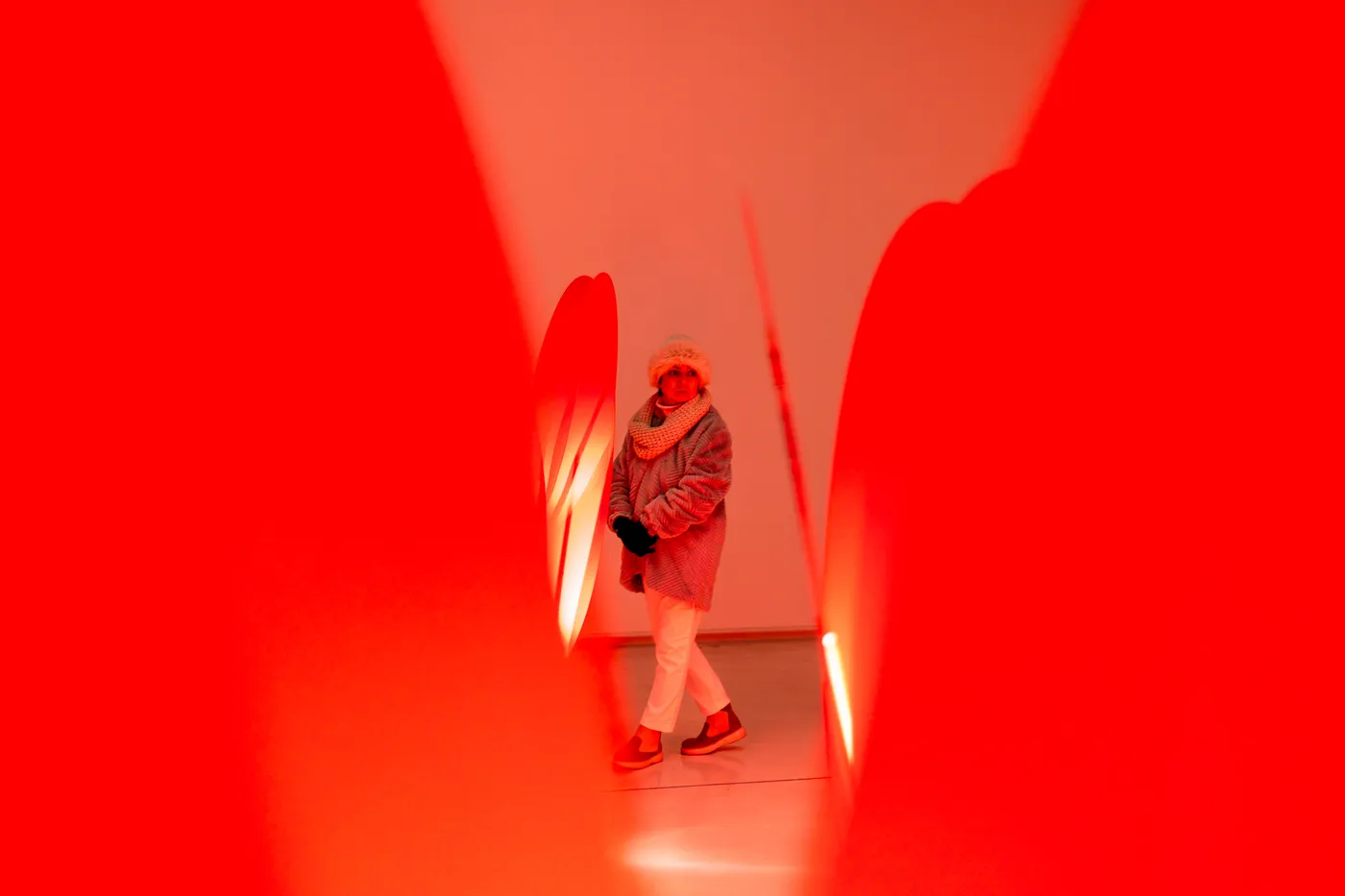 A visitor walking through rows of tall red tulip lamps in the red-lit gallery